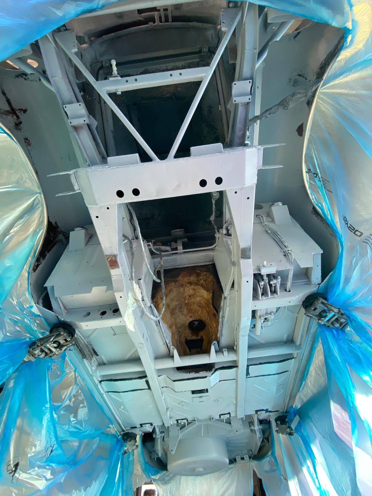 Une personne travaille sous un véhicule recouvert de plastique.