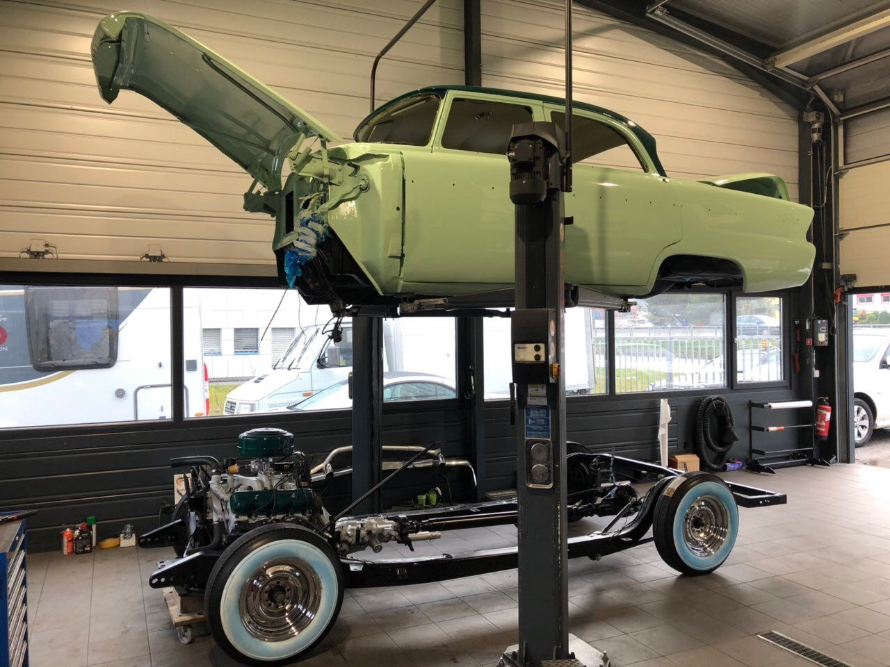 Carrosserie d'une voiture classique en vert pastel sur un pont élévateur dans le garage Universtyle Sion en phase de restauration