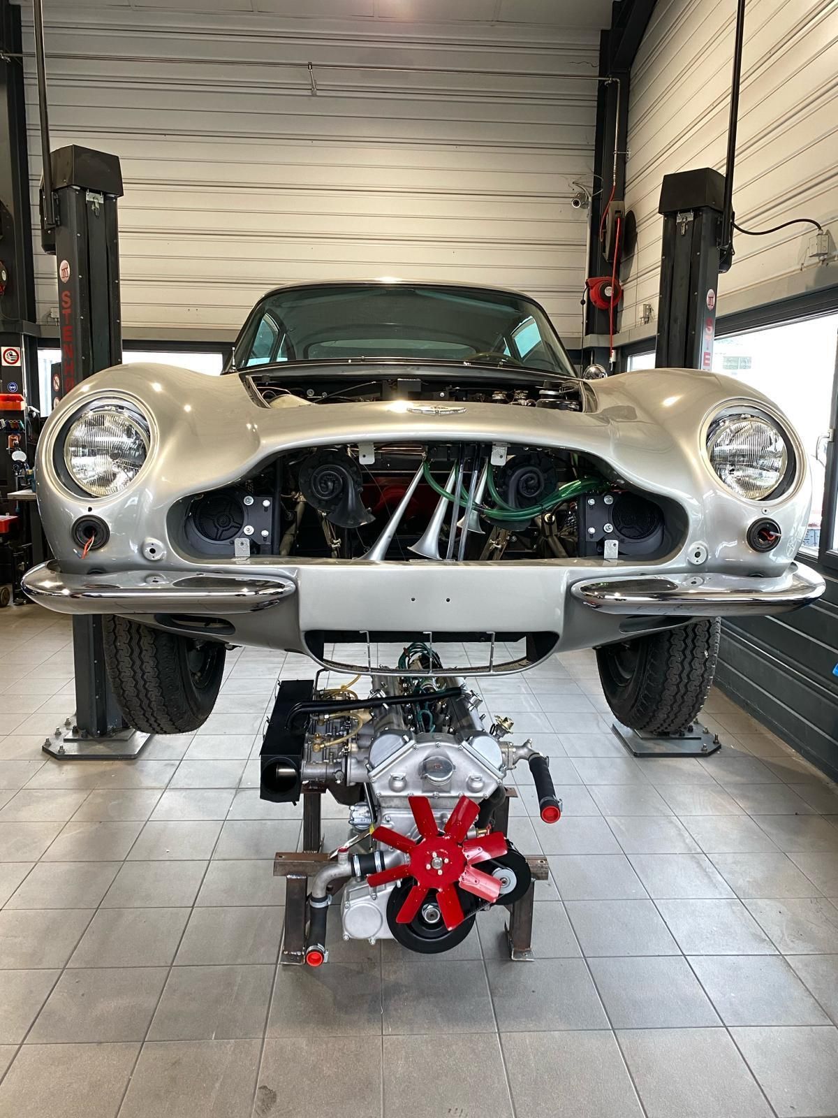 Une voiture argentée avec le capot relevé est sur un ascenseur dans un garage.