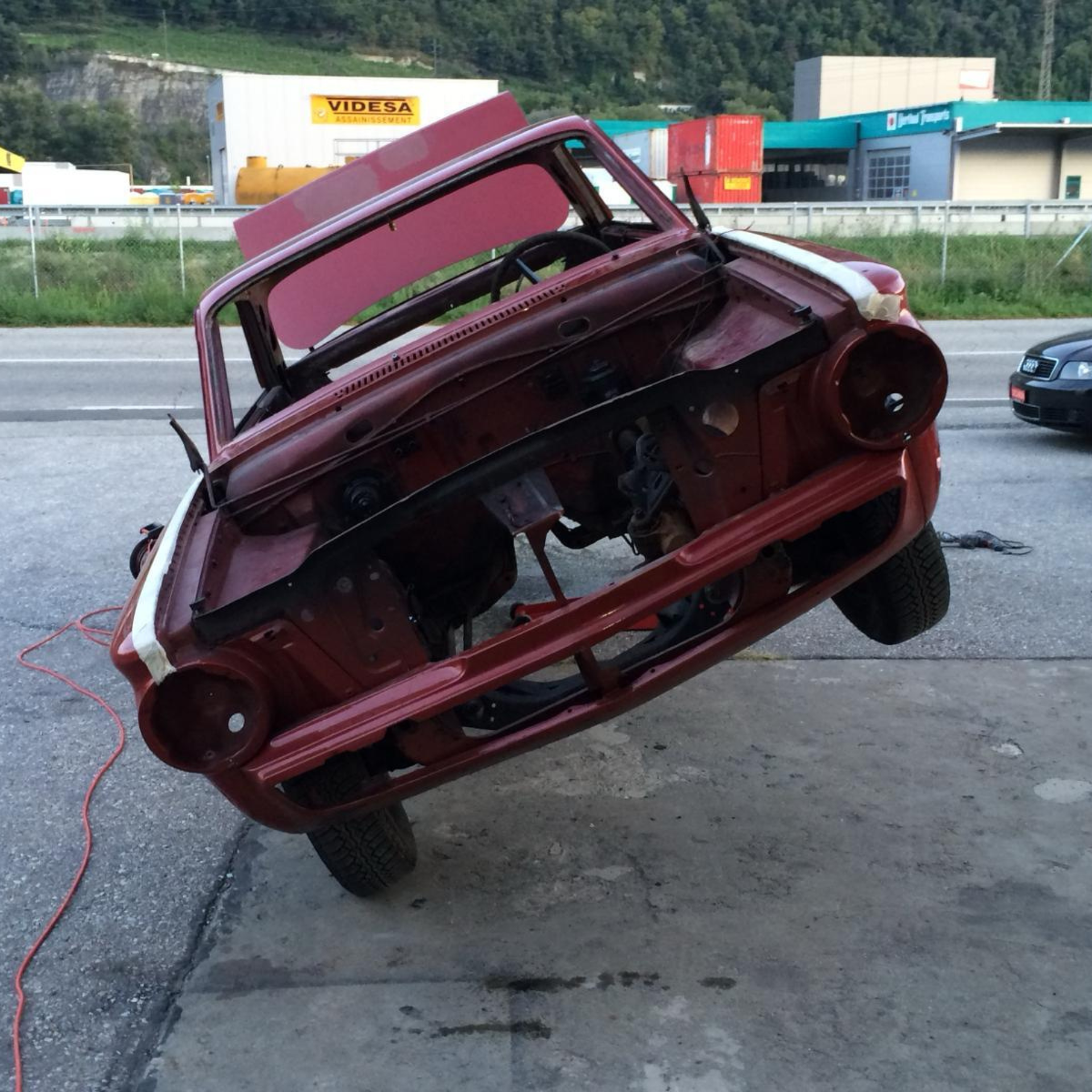 Une voiture rouge avec le capot relevé est garée sur le bord de la route