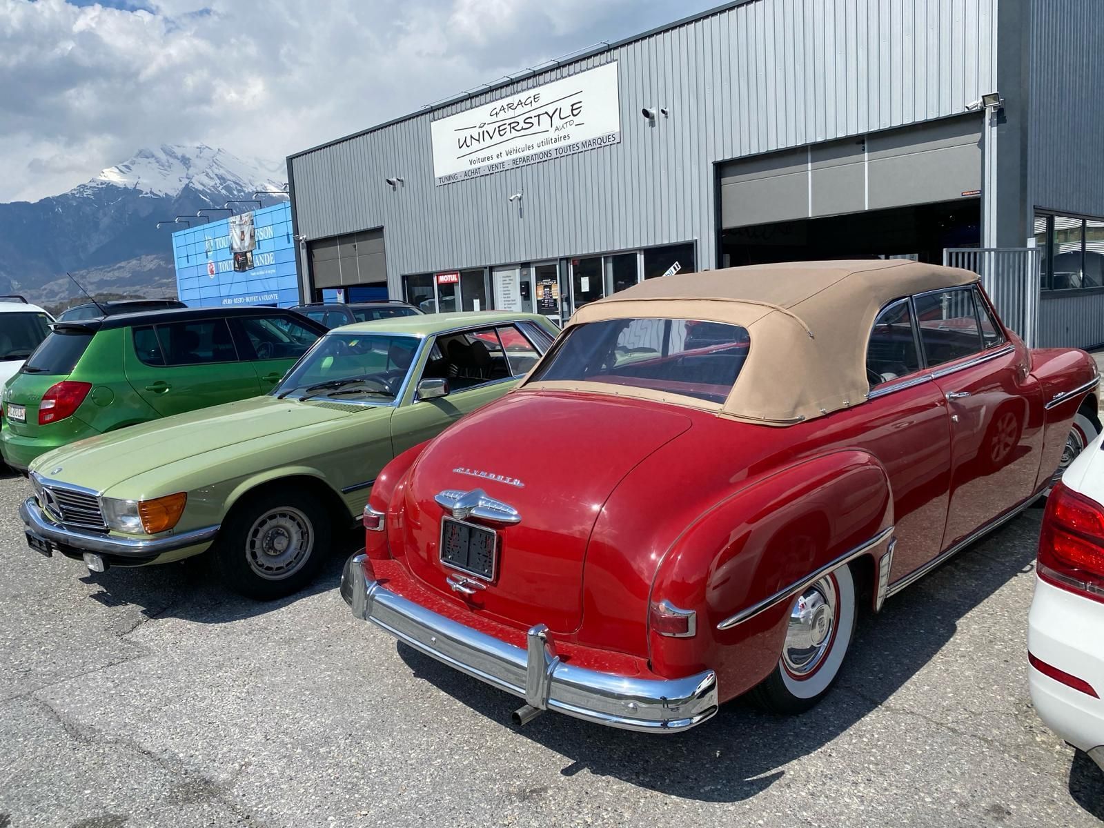 Mercedes-Benz classique rouge garée devant le garage Universtyle Sion avec montagnes suisse en arrière-plan