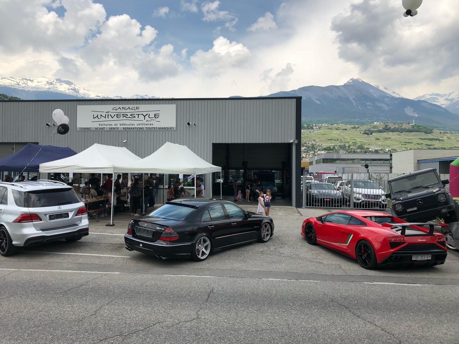 Vue extérieure du Garage Universtyle Sion avec un rassemblement de voitures de luxe et de clients lors d'un événement