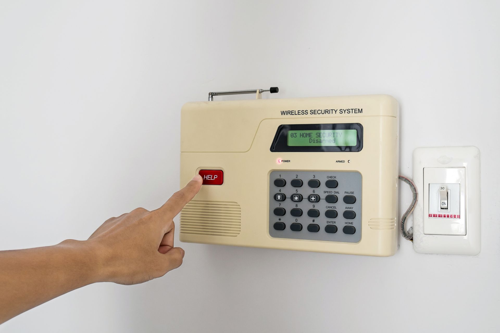 Person pressing a red button on a security alarm panel mounted on a white wall.