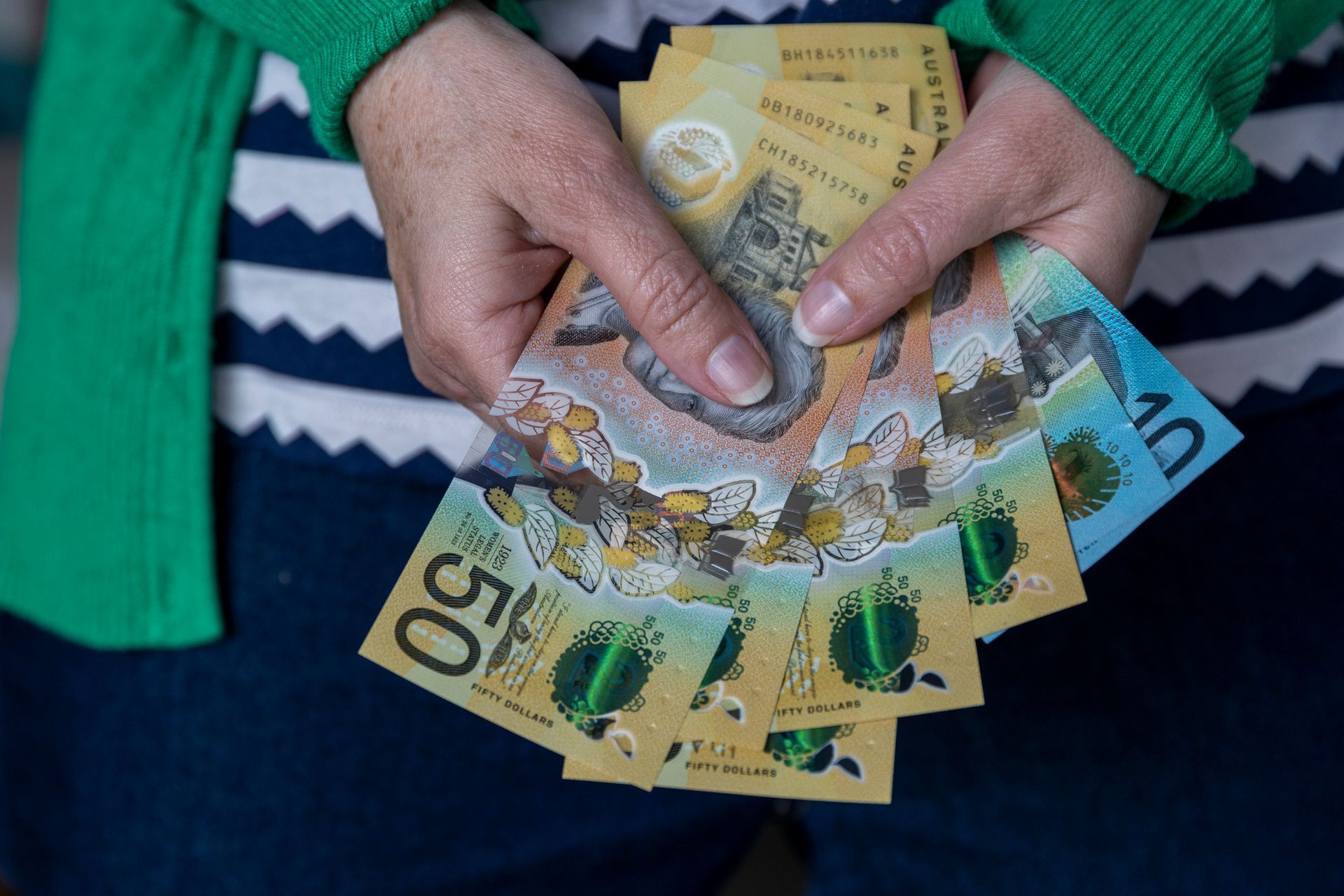 Hands holding Australian dollar banknotes: a mix of $50, $10, and other denominations.