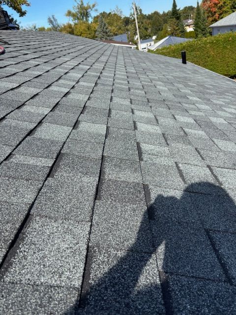 Vue rapprochée d'un toit en bardeaux d'asphalte gris par une journée ensoleillée avec l'ombre du photographe.