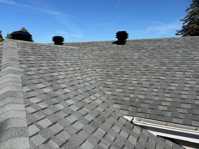 Toit en bardeaux d'asphalte gris avec des évents noirs contre un ciel bleu clair.