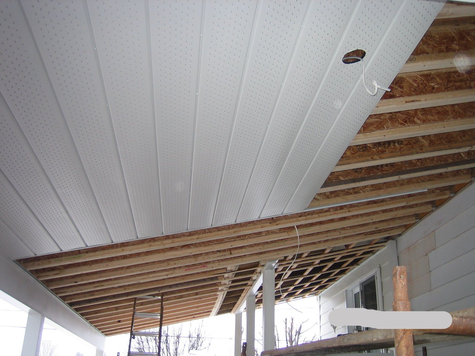 Panneaux de plafond blancs en cours d'installation sur des poutres en bois d'un porche.