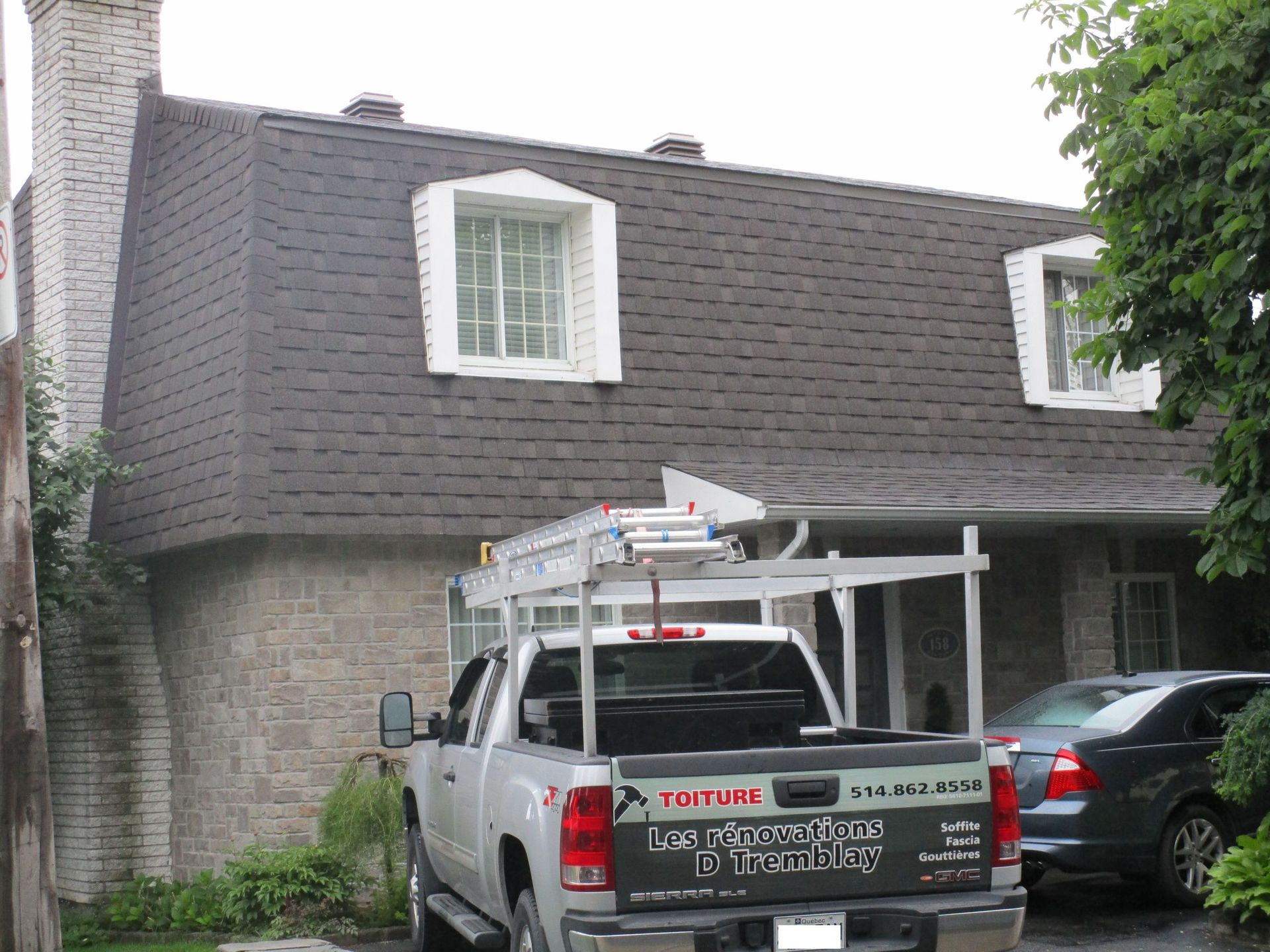 Maison au toit gris avec des lucarnes, à côté d'un camion avec un porte-échelle.