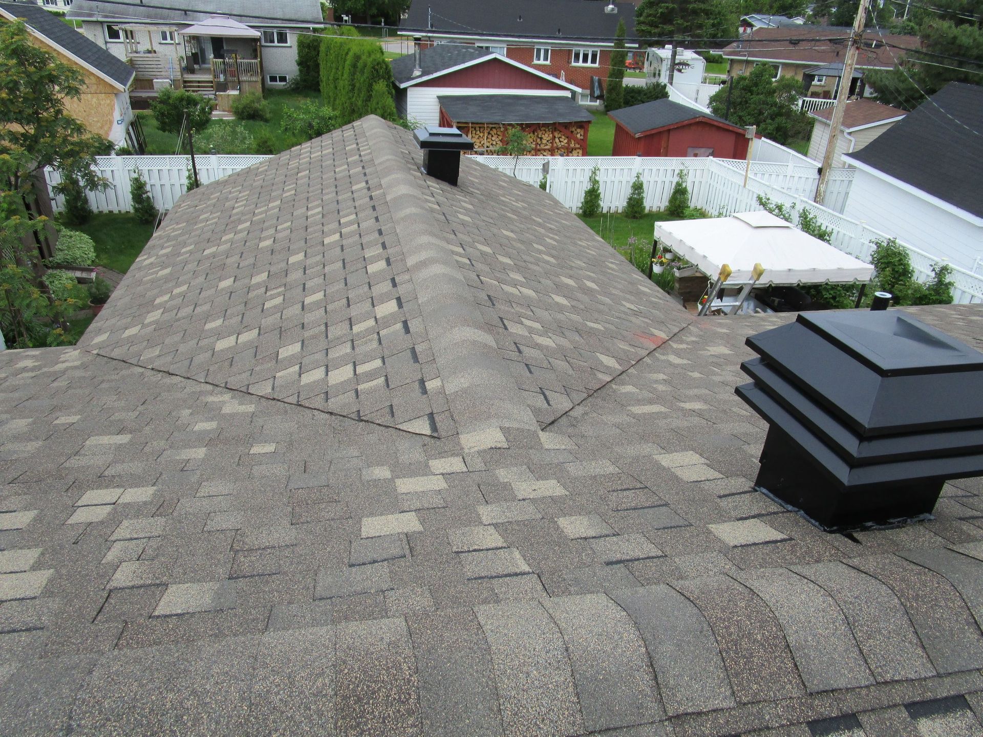 Toiture en bardeaux bruns avec deux cheminées noires, donnant sur un quartier résidentiel.