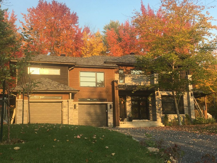 Maison moderne à deux étages avec garage, entourée d'arbres au feuillage d'automne rouge et orange.