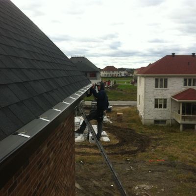 Personne sur une échelle installant une gouttière sur un bâtiment en briques au toit sombre. Cadre suburbain.