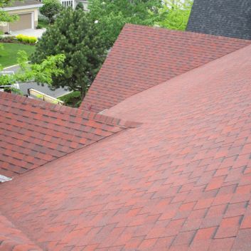 Toit en bardeaux rouges d'une maison à plusieurs sections et arbres verts en arrière-plan.