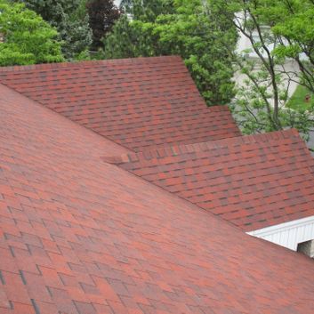 Toit en bardeaux rouges avec plusieurs sections et arbres verts en arrière-plan.