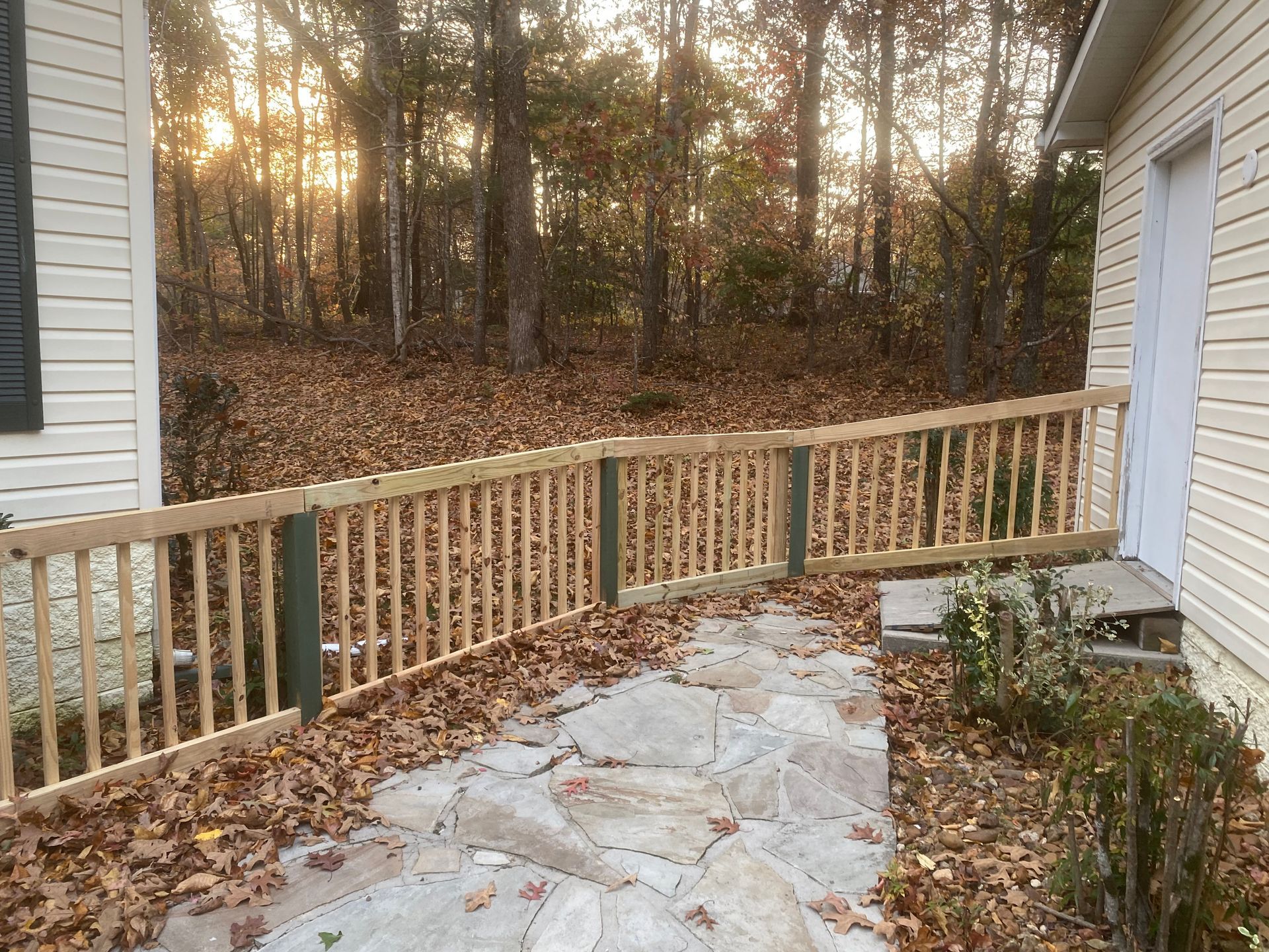 A wooden fence surrounds a stone walkway leading to a house.