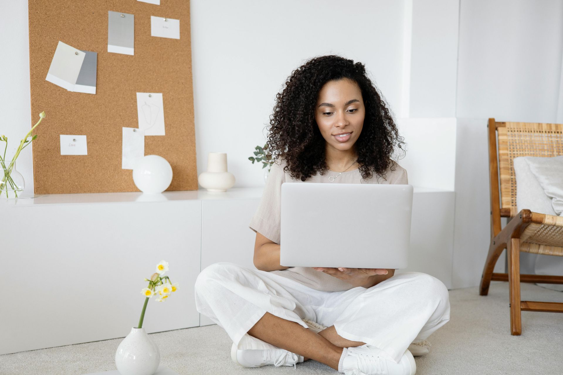 Woman with hands on chin looks at laptop screen in front of brick wall.