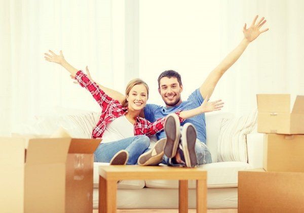 A man and a woman are sitting on a couch with their arms in the air.