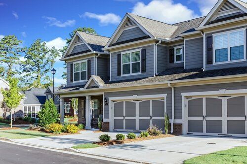 A large gray house with two garage doors is sitting on the corner of a residential street.