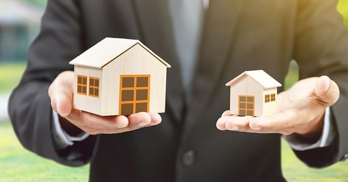A man in a suit is holding two small houses in his hands.