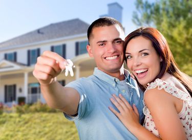 A man and woman are standing in front of a house holding keys.