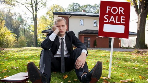 A man is sitting in front of a for sale sign
