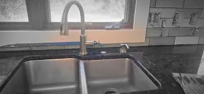A kitchen sink with a faucet and a window in the background.