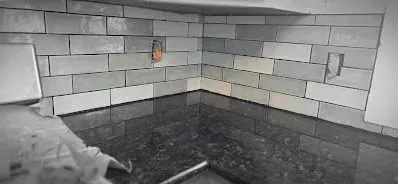 A black and white photo of a kitchen with brick tiles and a black counter top.