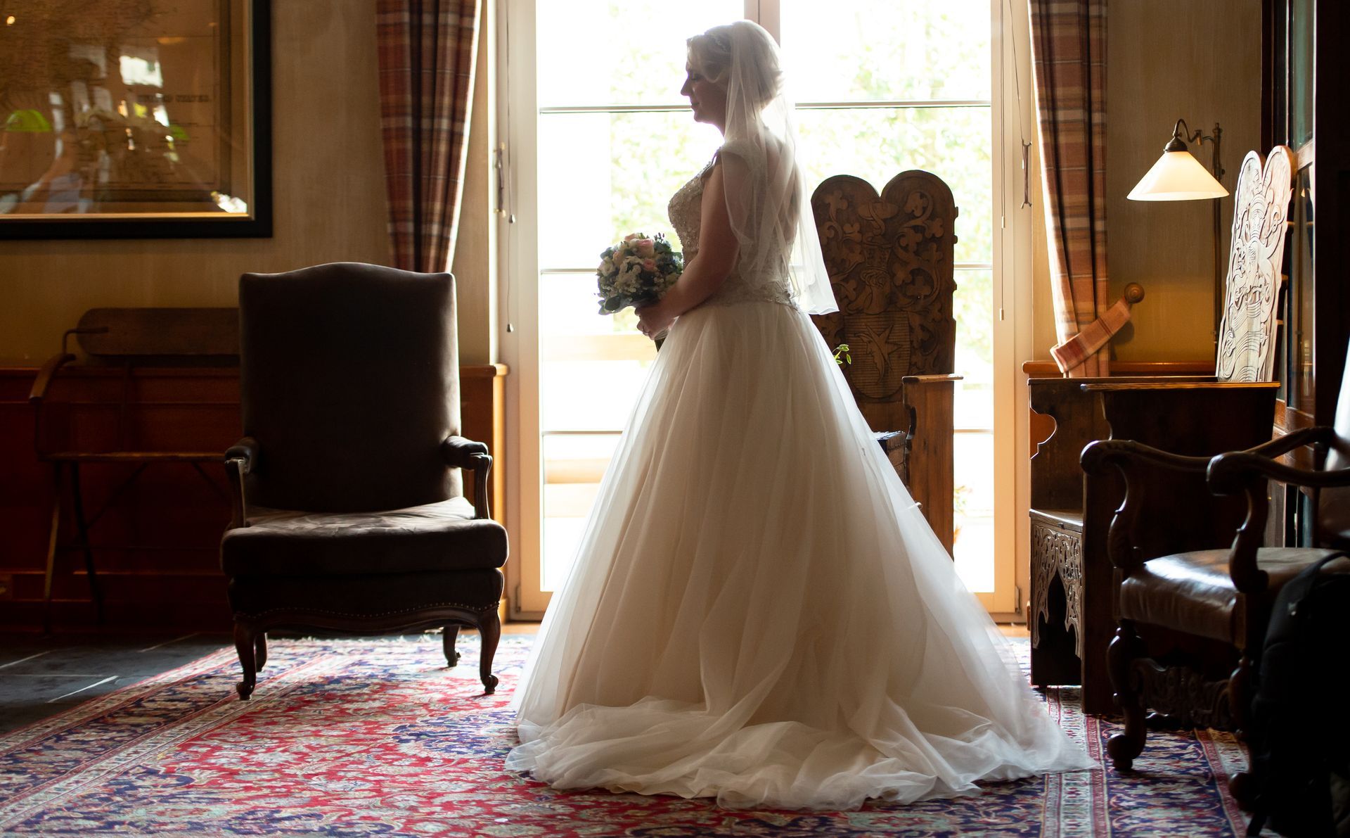 A bride in a wedding dress is standing in a room holding a bouquet of flowers.