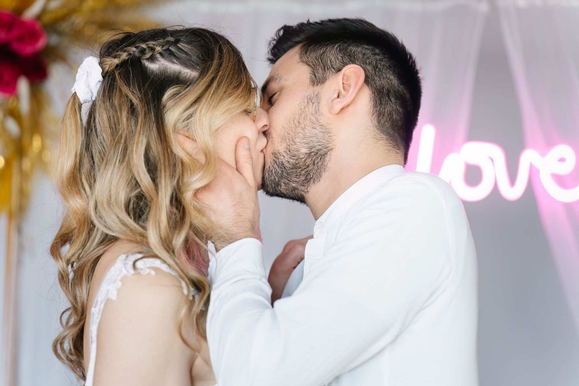 A man and a woman are kissing in front of a neon sign that says love.