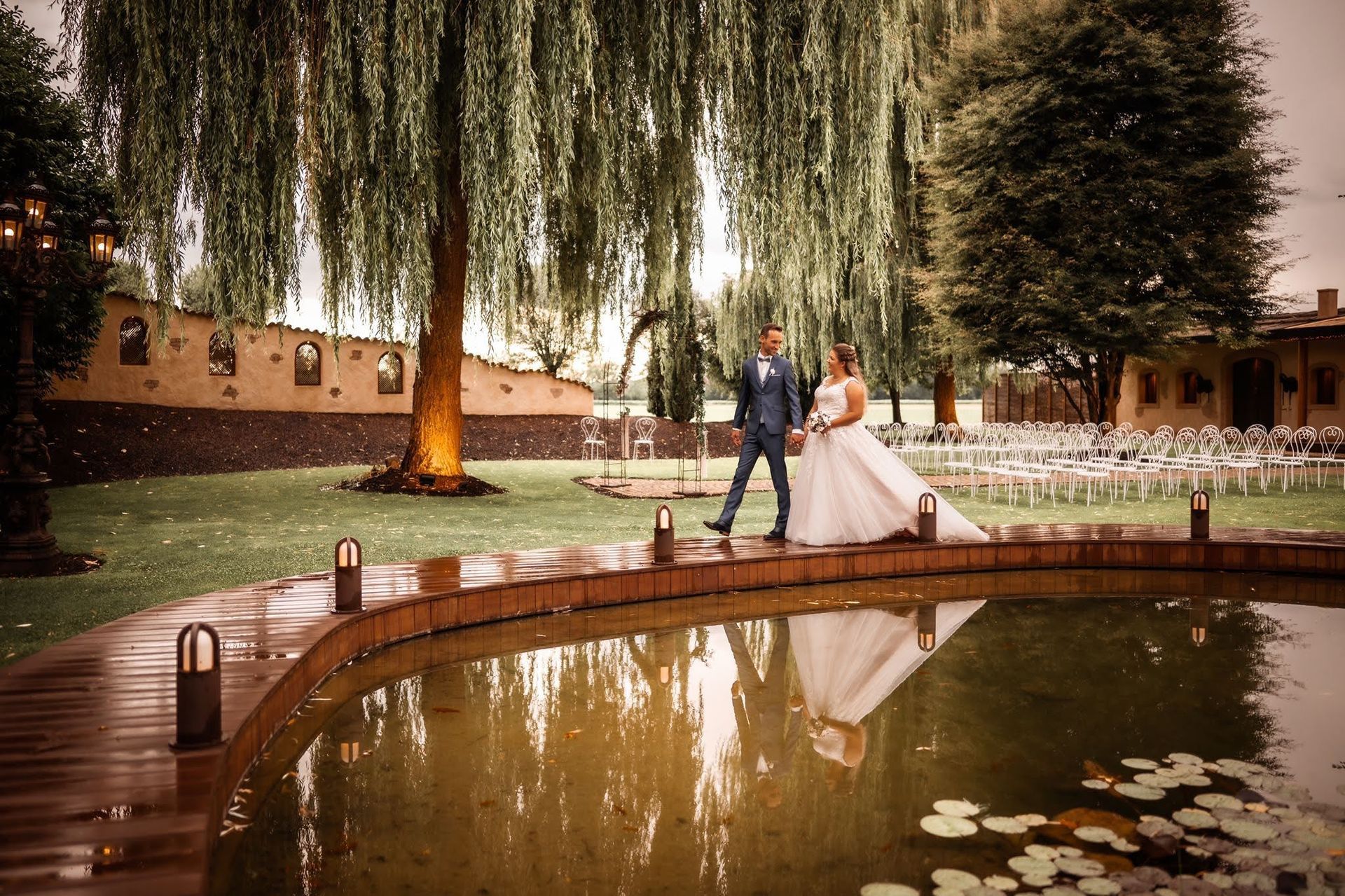 A bride and groom are standing next to a pond.