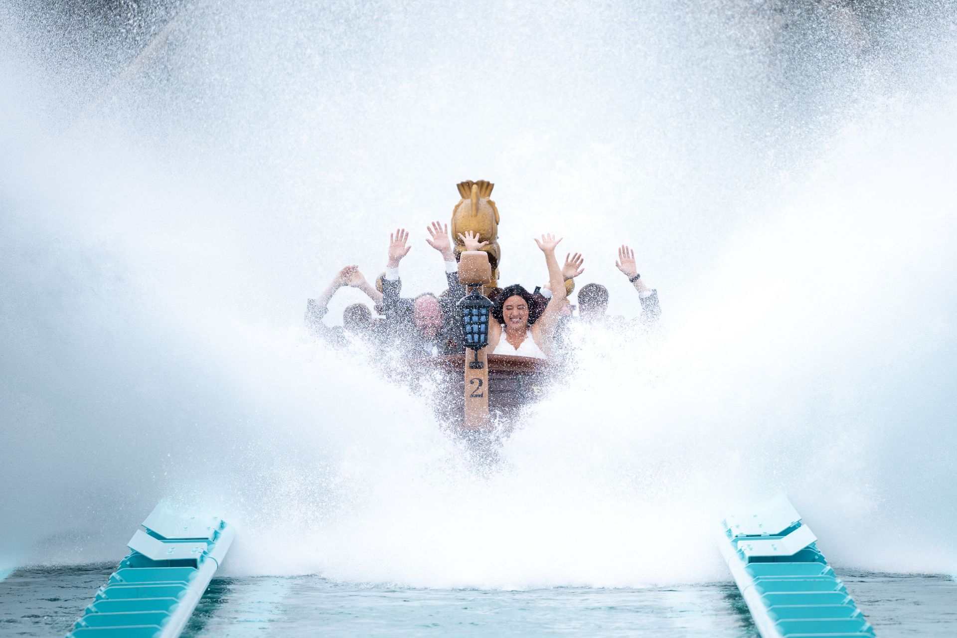 People on a log flume ride are drenched in a huge splash of water, raising their arms in excitement.