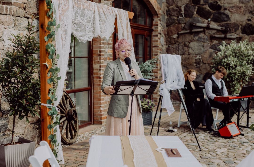 A woman is giving a speech at a wedding while a man plays a keyboard.