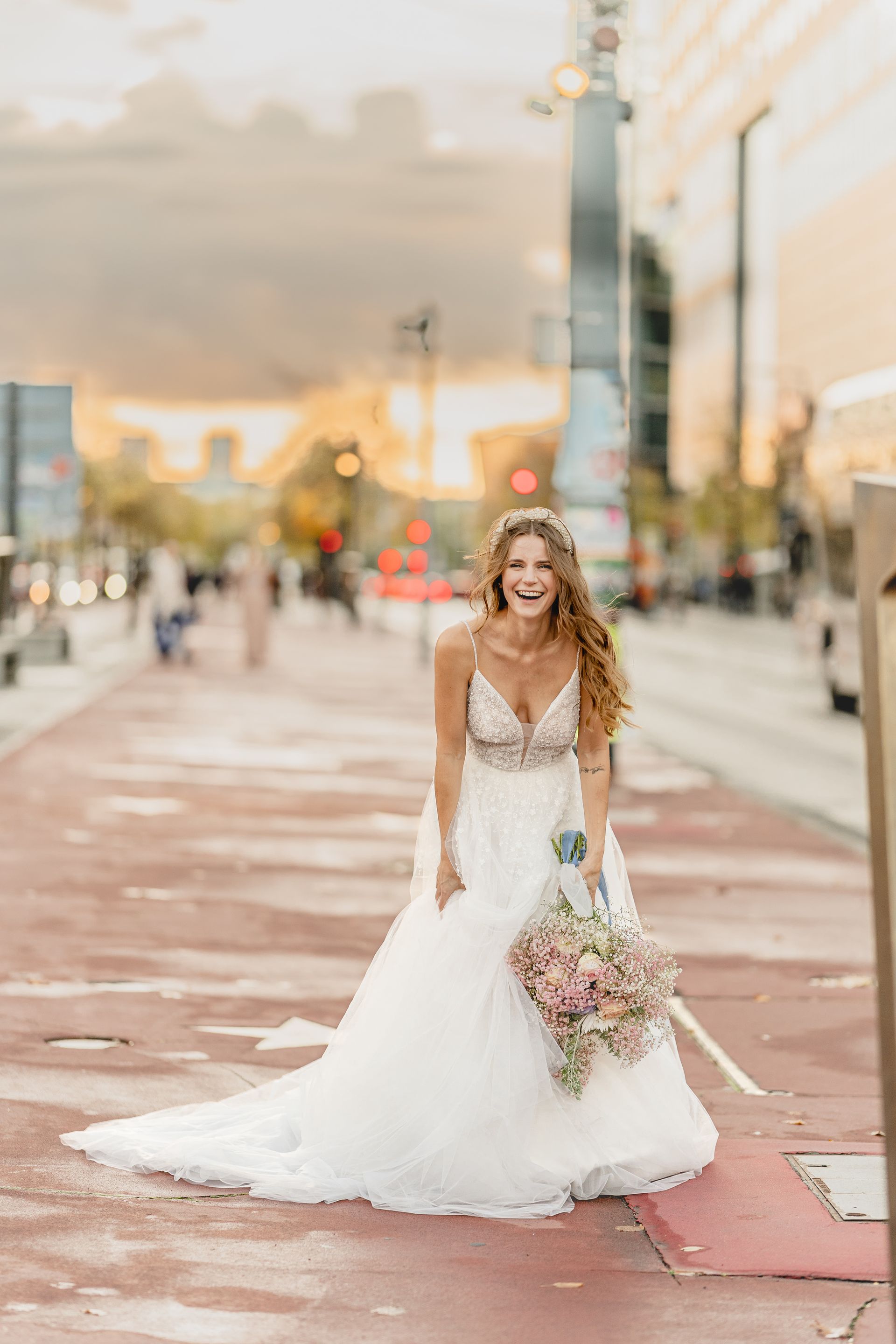 A bride in a wedding dress is standing on a sidewalk holding a bouquet of flowers.