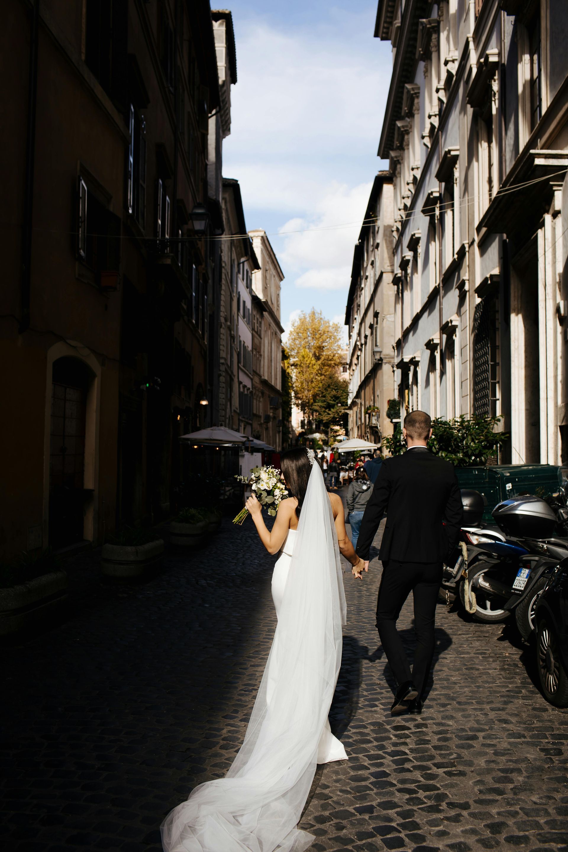 A bride and groom are walking down a cobblestone street holding hands.