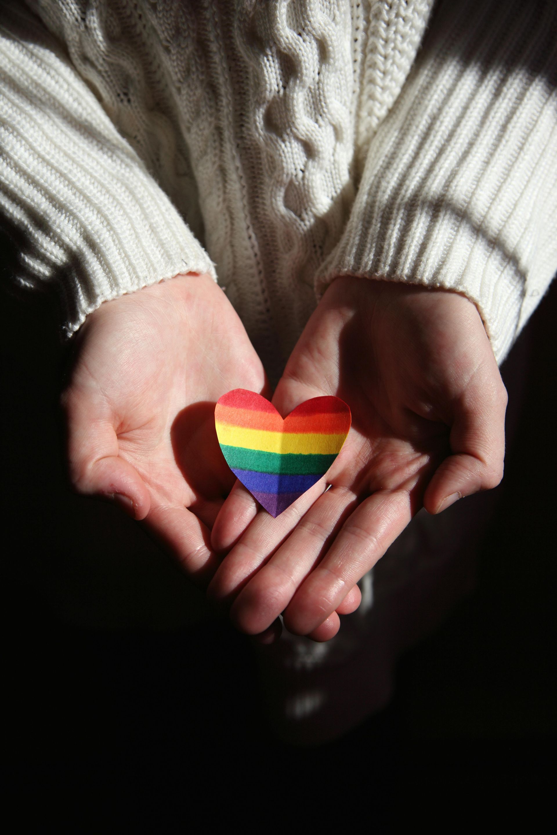 Hands cupped, holding a small, rainbow-colored heart, symbolizing LGBTQ+ pride.
