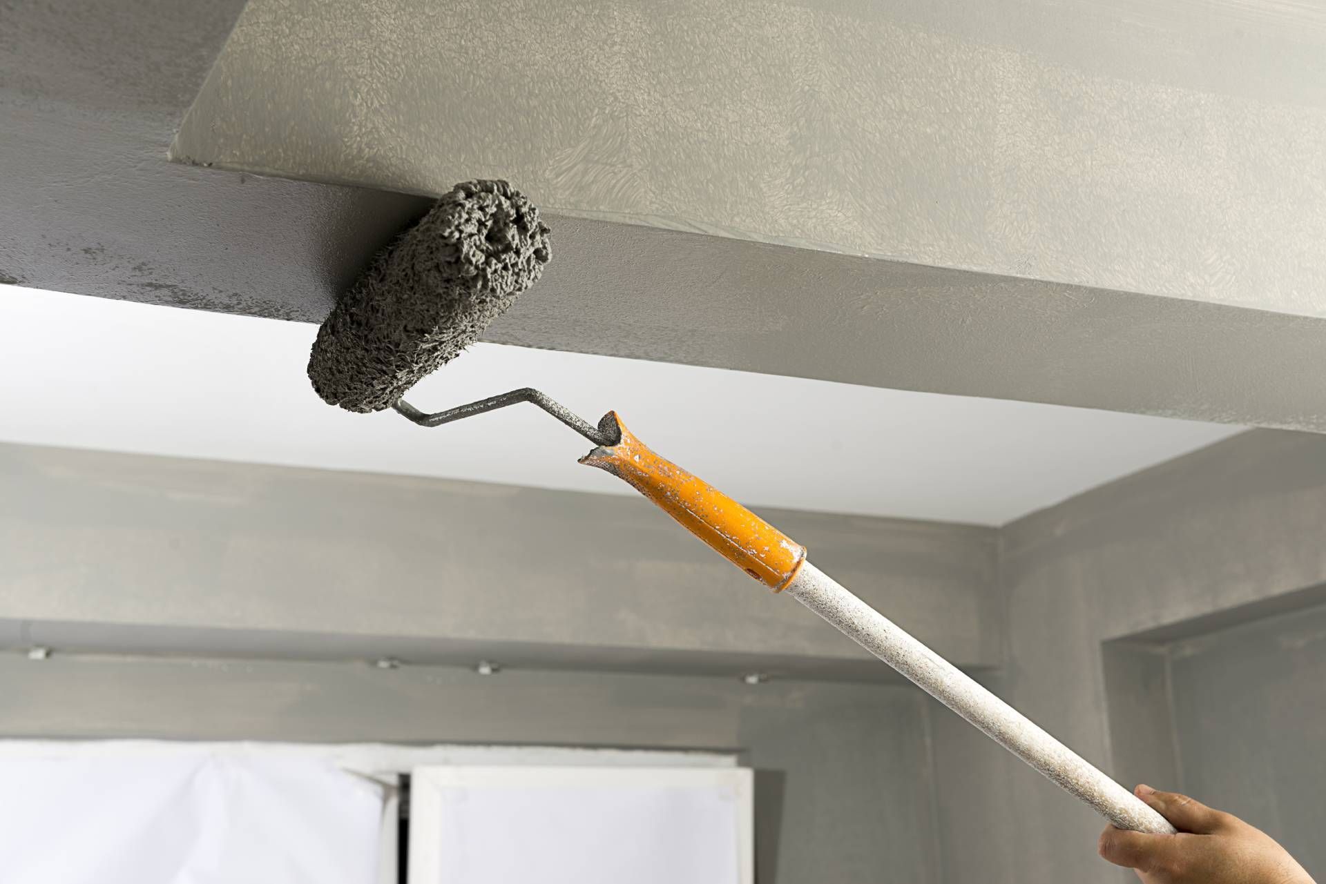 Person painting a gray ceiling with a paint roller on an extended handle.