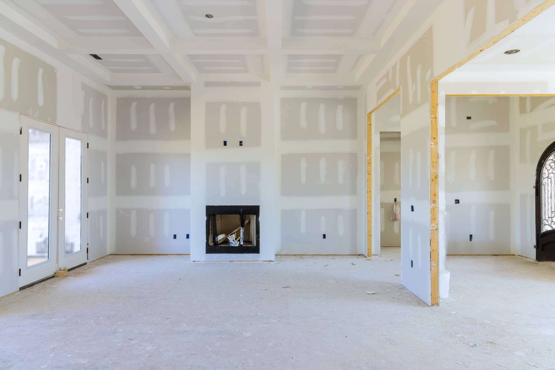 Interior of a room under construction, with drywall covering walls and ceiling; fireplace, doorways.