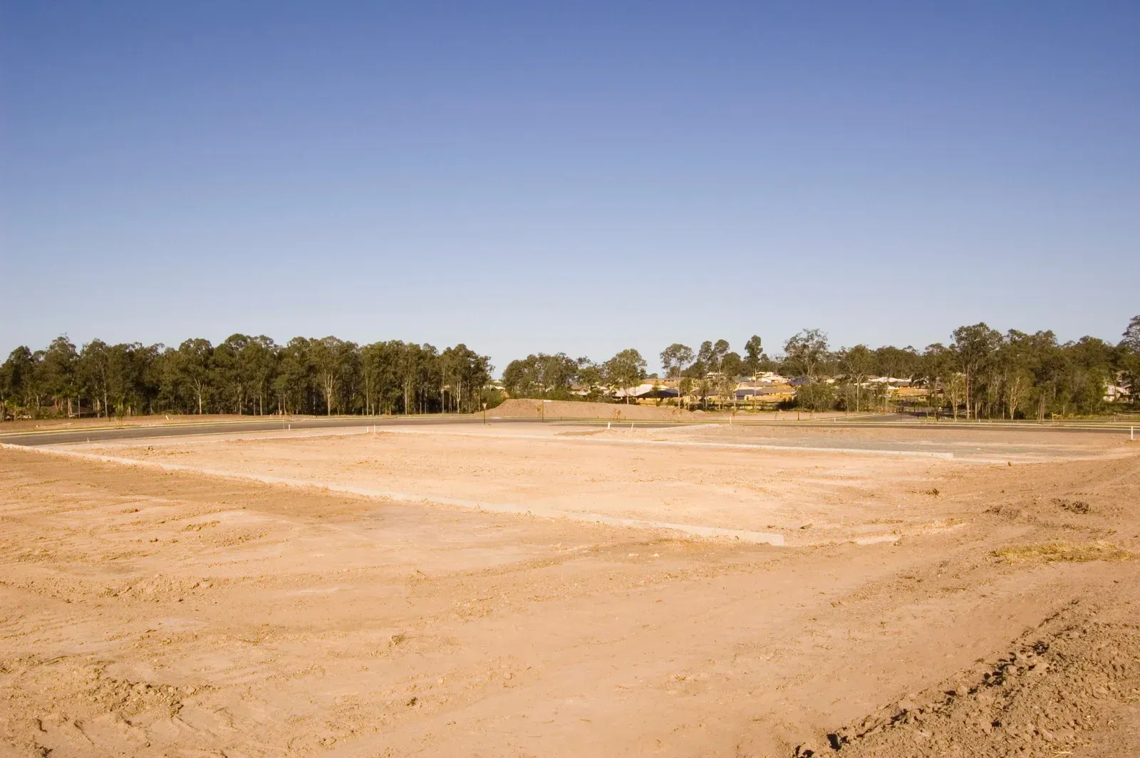 An empty field with trees in the background and a blue sky