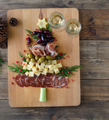 A charcuterie board arranged into the shape of a Christmas tree with meat, cheese, grapes, olives, and a leek trunk.