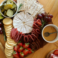 An overhead shot of a charcuterie board featuring cheese, crackers, salami, grapes, strawberries, pickles, and dip.