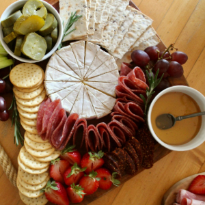 An overhead shot of a charcuterie board featuring cheese, crackers, salami, grapes, strawberries, pickles, and dip.