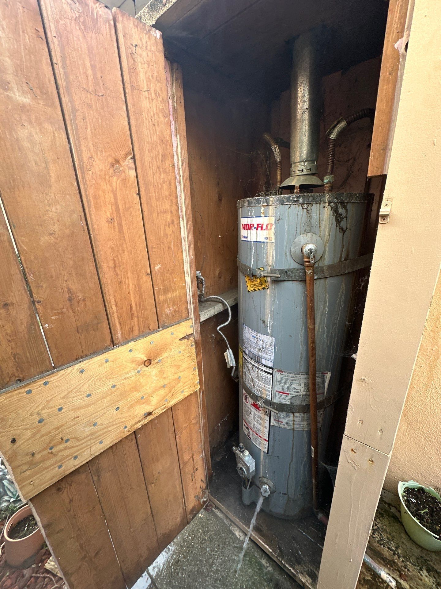 Water heater in a narrow wooden utility closet, with pipes and labels visible.