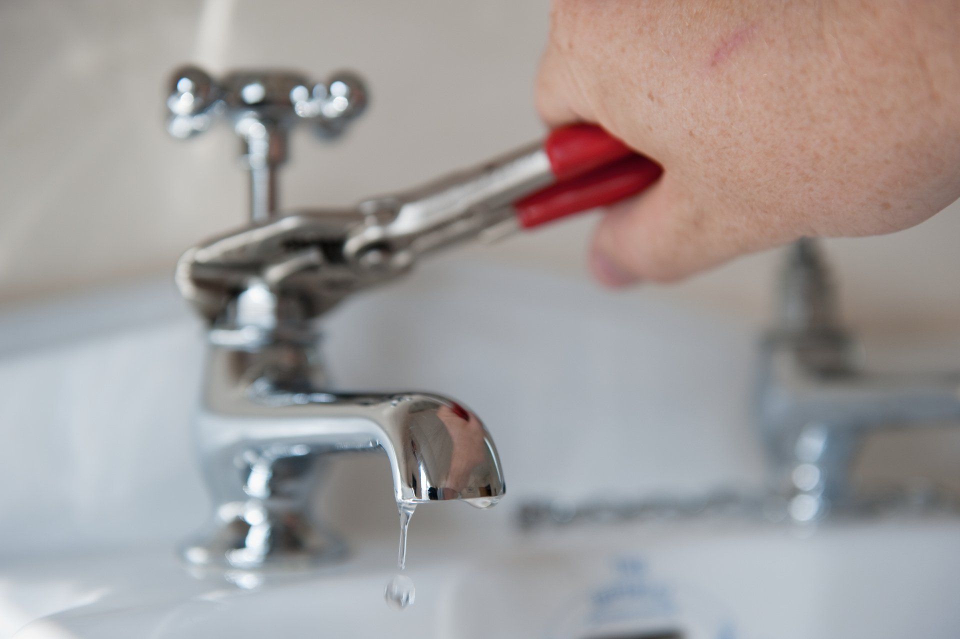 Person using a red toothbrush to brush teeth at a bathroom sink, water dripping from faucet