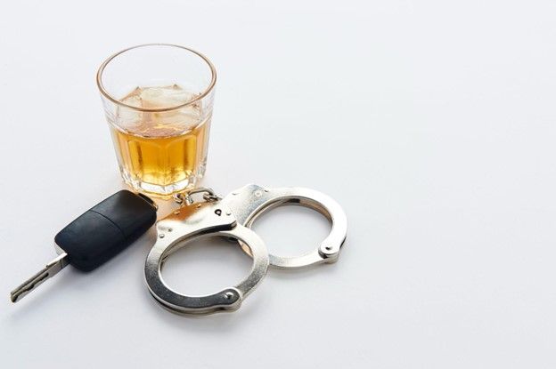 A car key , handcuffs , and a glass of alcohol on a white background.