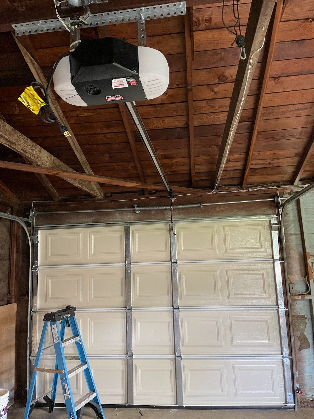 A garage door opener is hanging from the ceiling above a garage door.