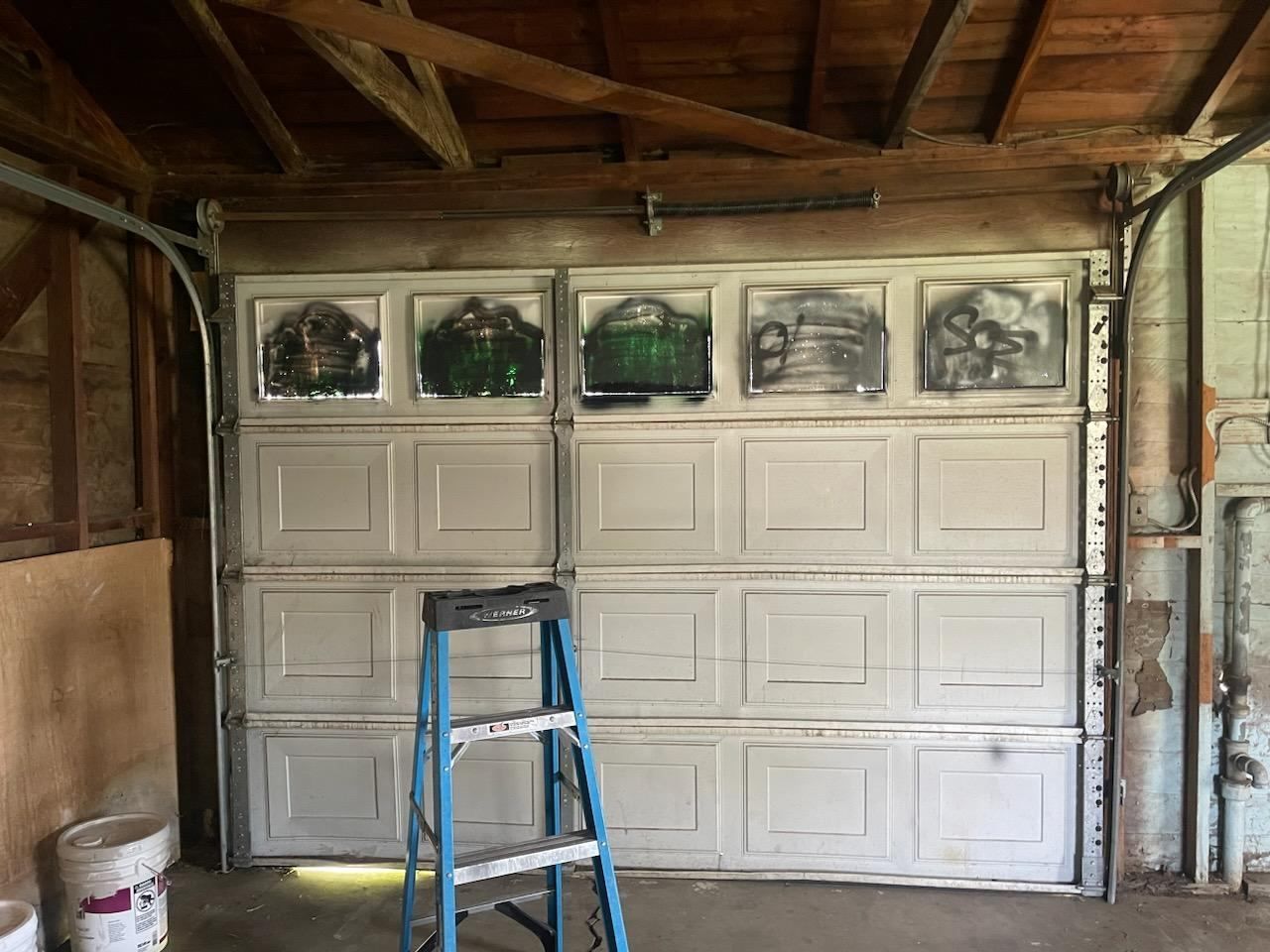 A garage door with graffiti on it and a ladder in front of it.