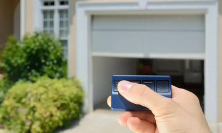 A person is holding a remote control in front of a garage door.
