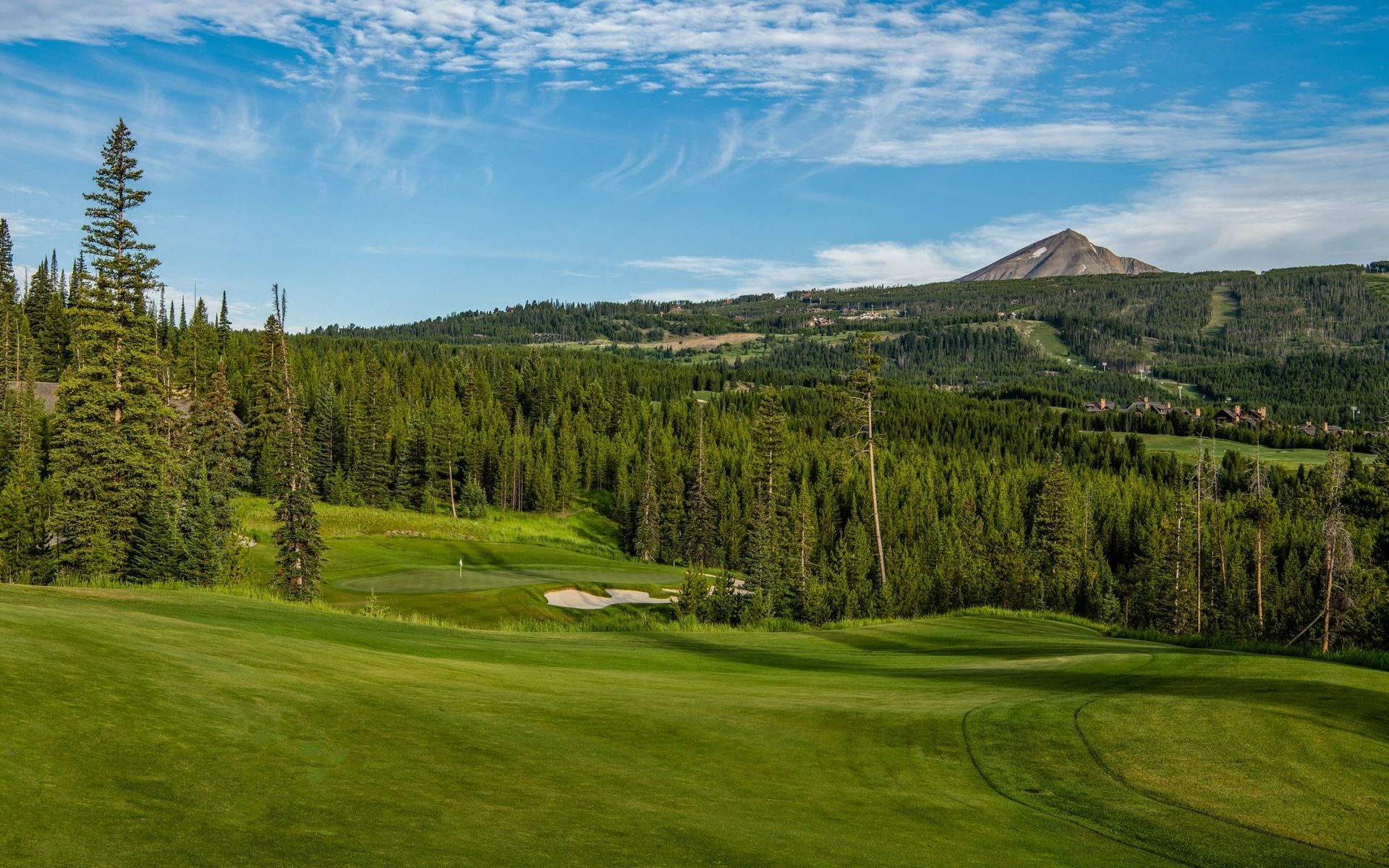 A golf course with a mountain in the background and trees in the foreground.