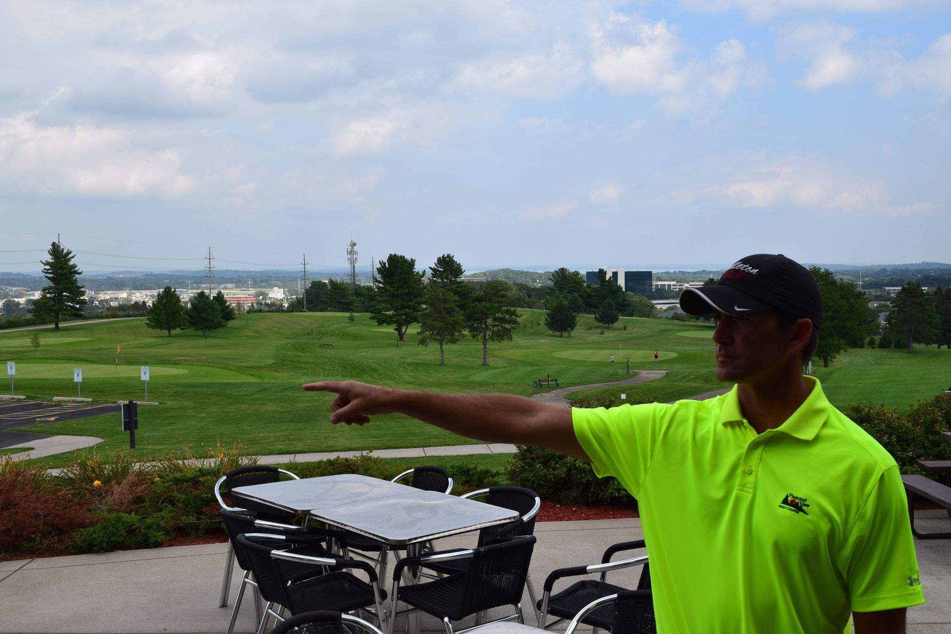 A man in a neon yellow shirt is pointing at a golf course.