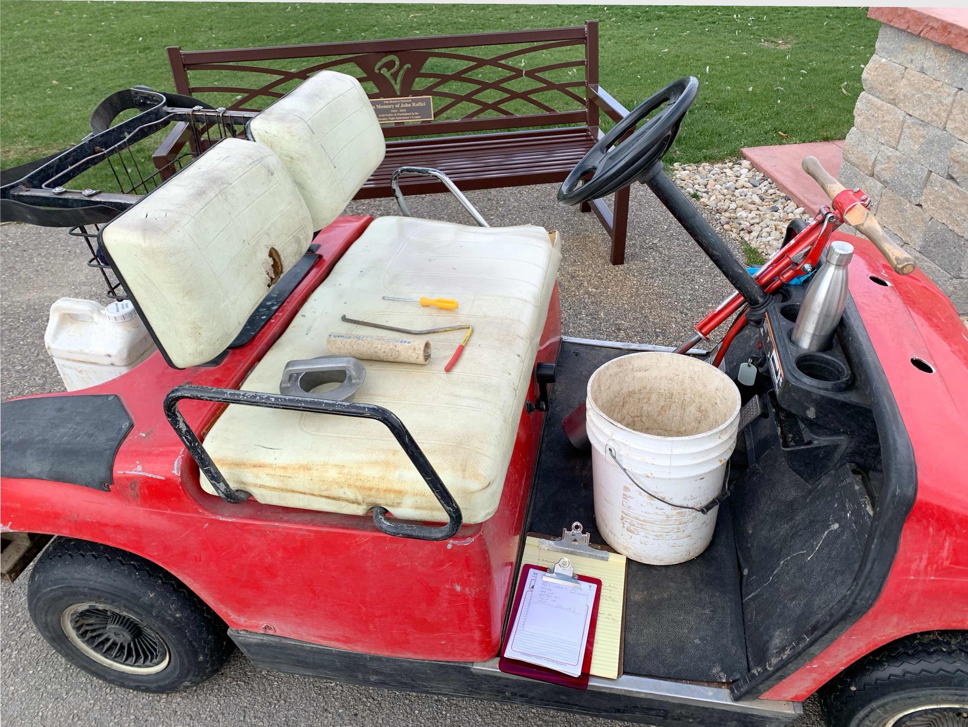 A red golf cart is parked next to a bench