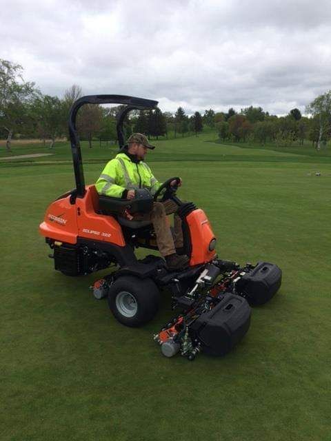 A man is riding an orange lawn mower on a golf course